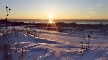 Paisaje nevado con el sol poniéndose sobre un terreno llano, vegetación escasa y horizonte despejado.
