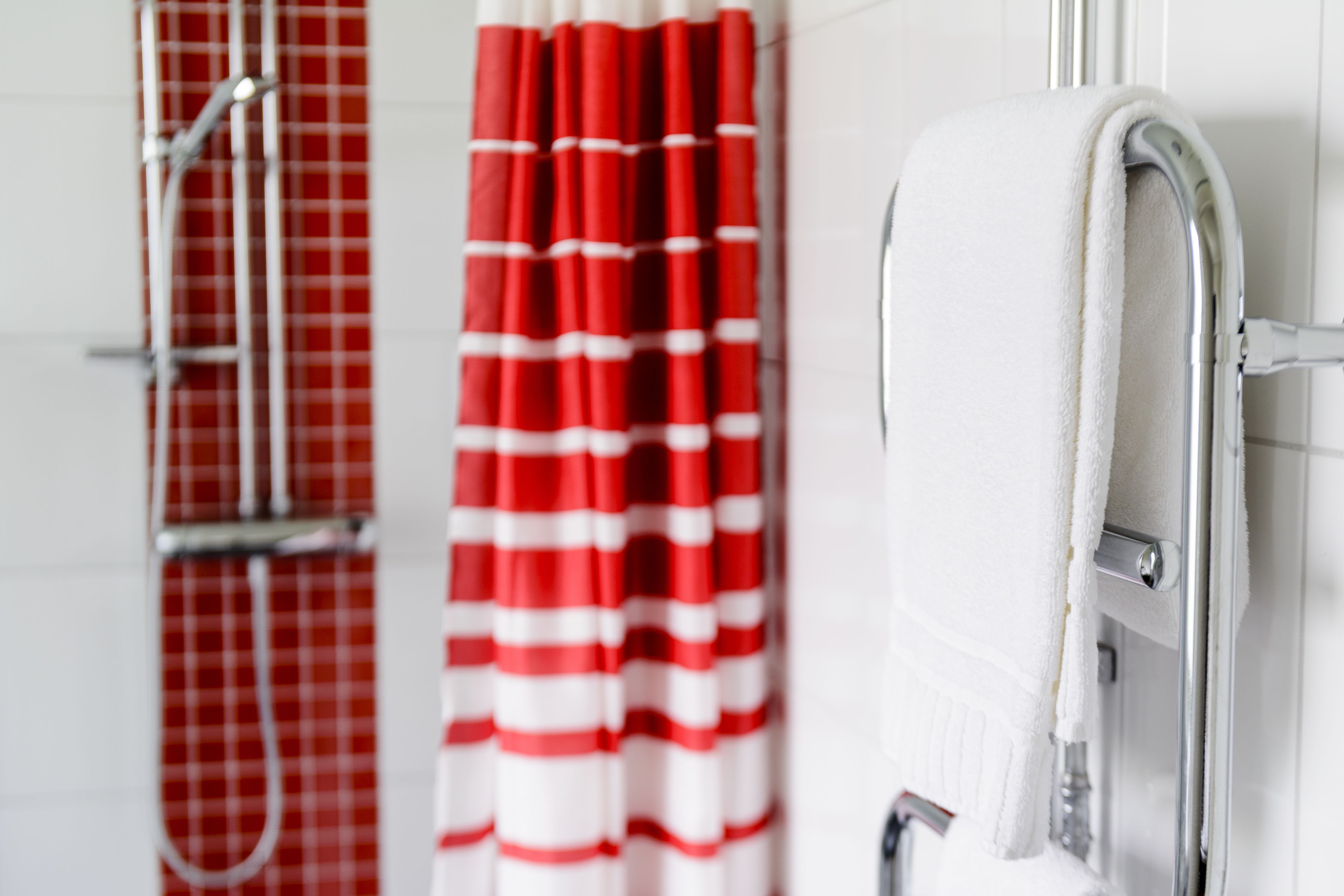 A bathroom with a shower, a red and white striped shower curtain, and a white towel hanging on a metal towel rack.