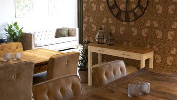 Een eetruimte met een houten tafel en stoelen, een klok aan de muur en behang met een patroon.
