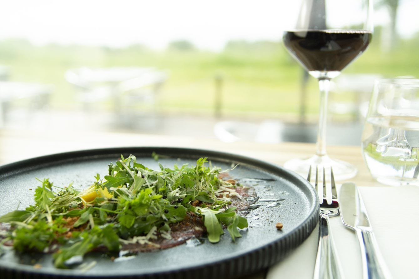 A plate of food with greens and a glass of red wine on a table.