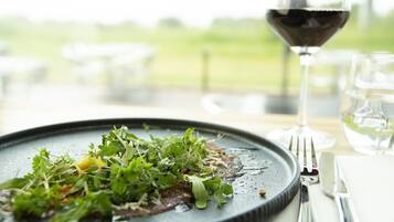 A plate of food with greens and a glass of red wine on a table.