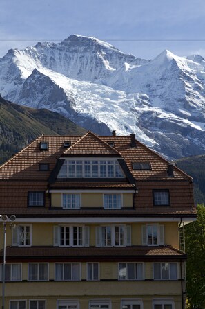 A two-story building with a sloped roof and multiple windows, set against a backdrop of snow-capped mountains. - Apartement Silverpeak (Lauterbrunnen)