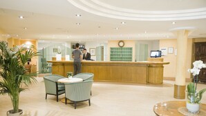 Un hall de hotel con mostrador de recepción, zona de estar y una pantalla de televisión.