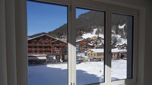 Vista desde una ventana de un edificio con varios balcones, un paisaje nevado y una montaña al fondo.