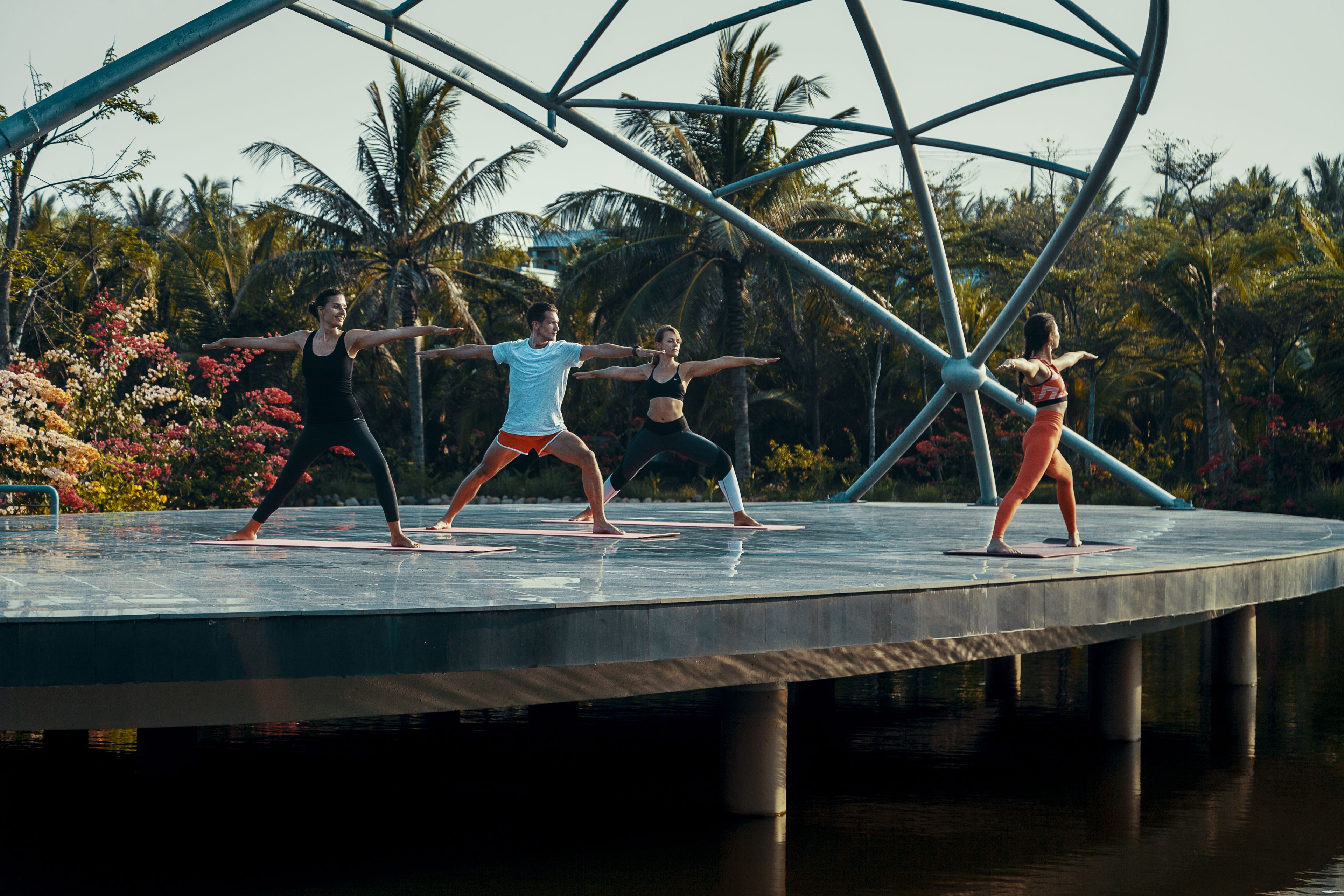 A group performing on a circular stage with a water feature below, surrounded by palm trees and colorful flowers.