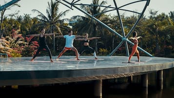 A group performing on a circular stage with a water feature below, surrounded by palm trees and colorful flowers.