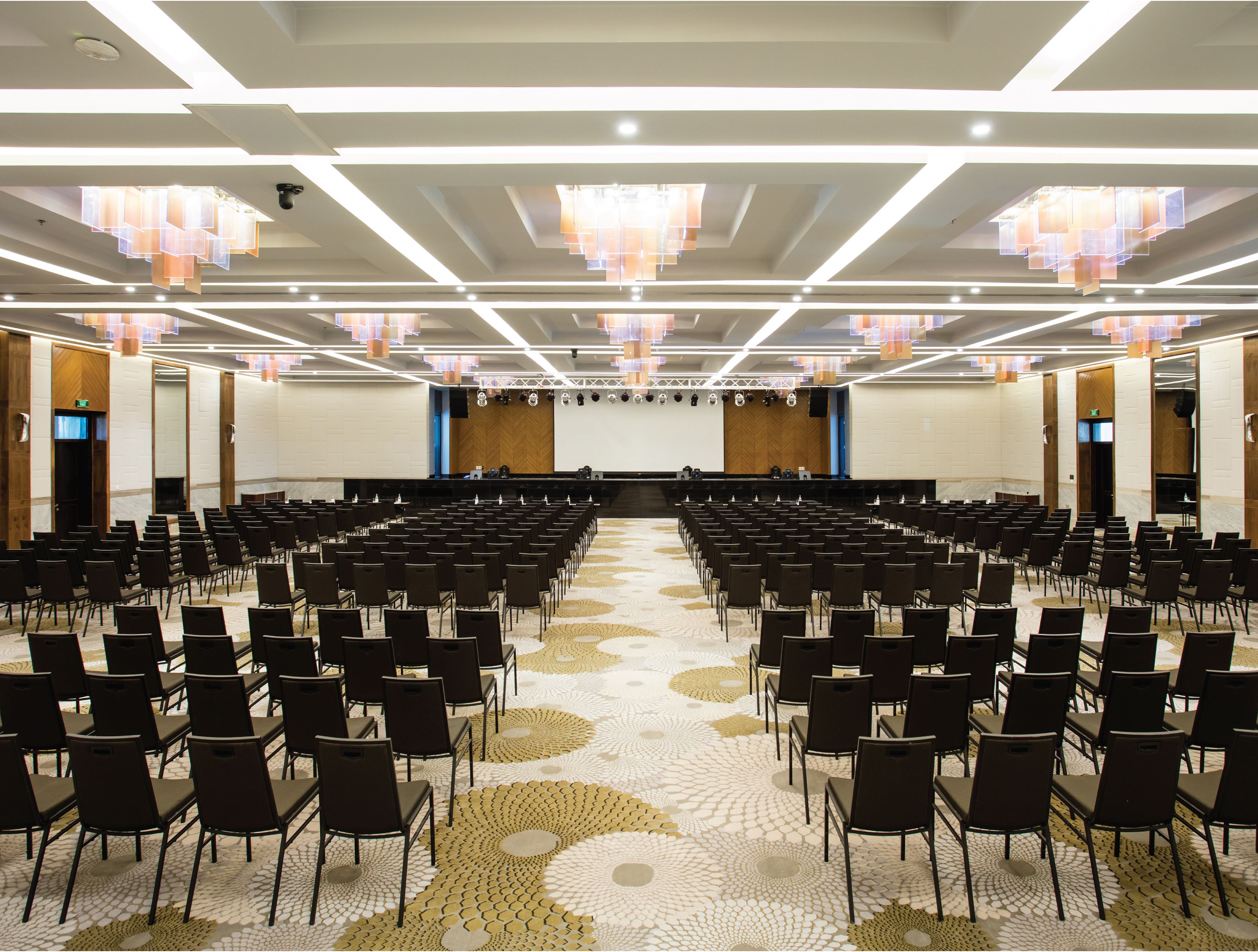 A conference room with rows of chairs facing a stage, equipped with a sound system and a large screen.