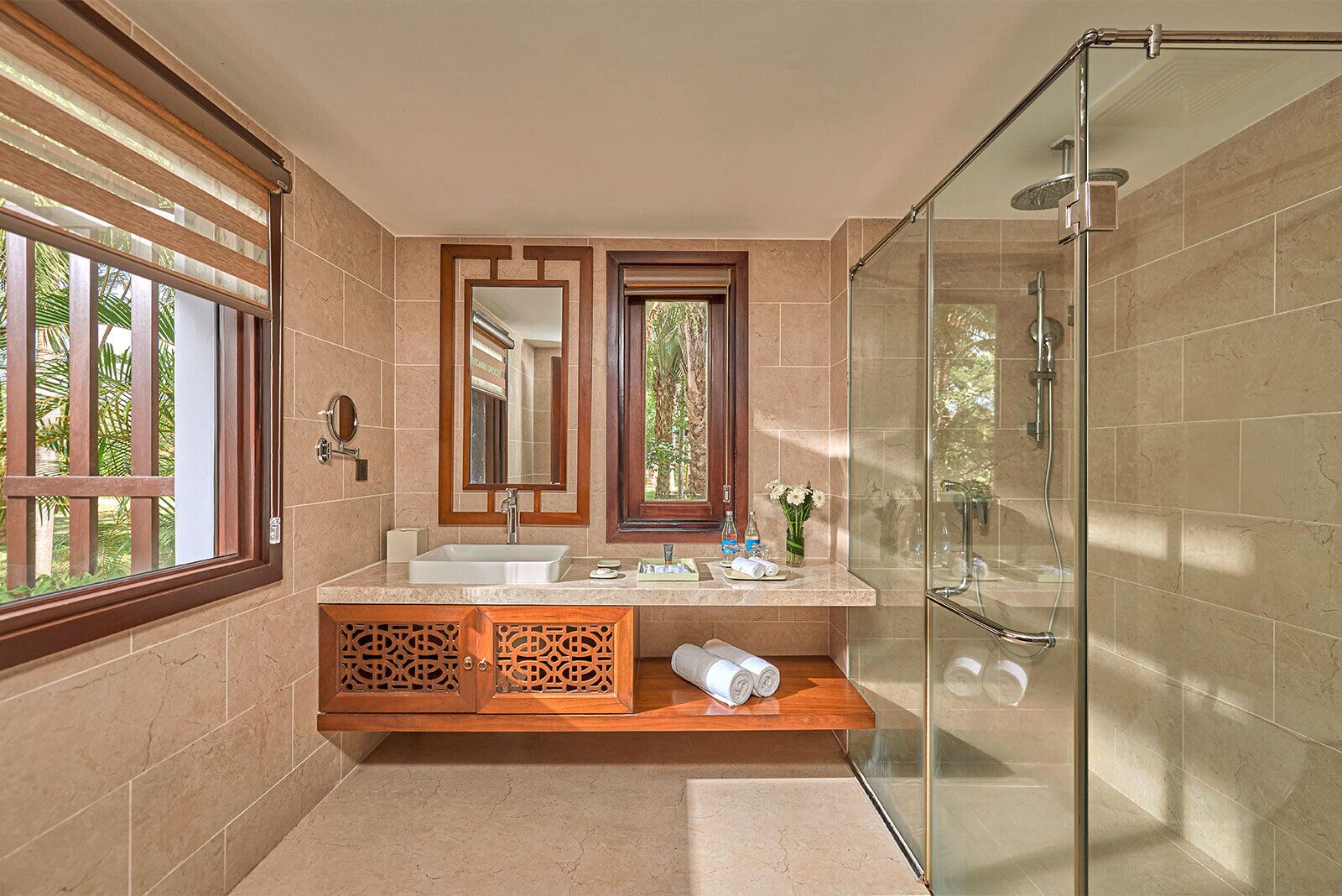 A bathroom with two sinks, a large mirror, a shower, and a window with a view of greenery.