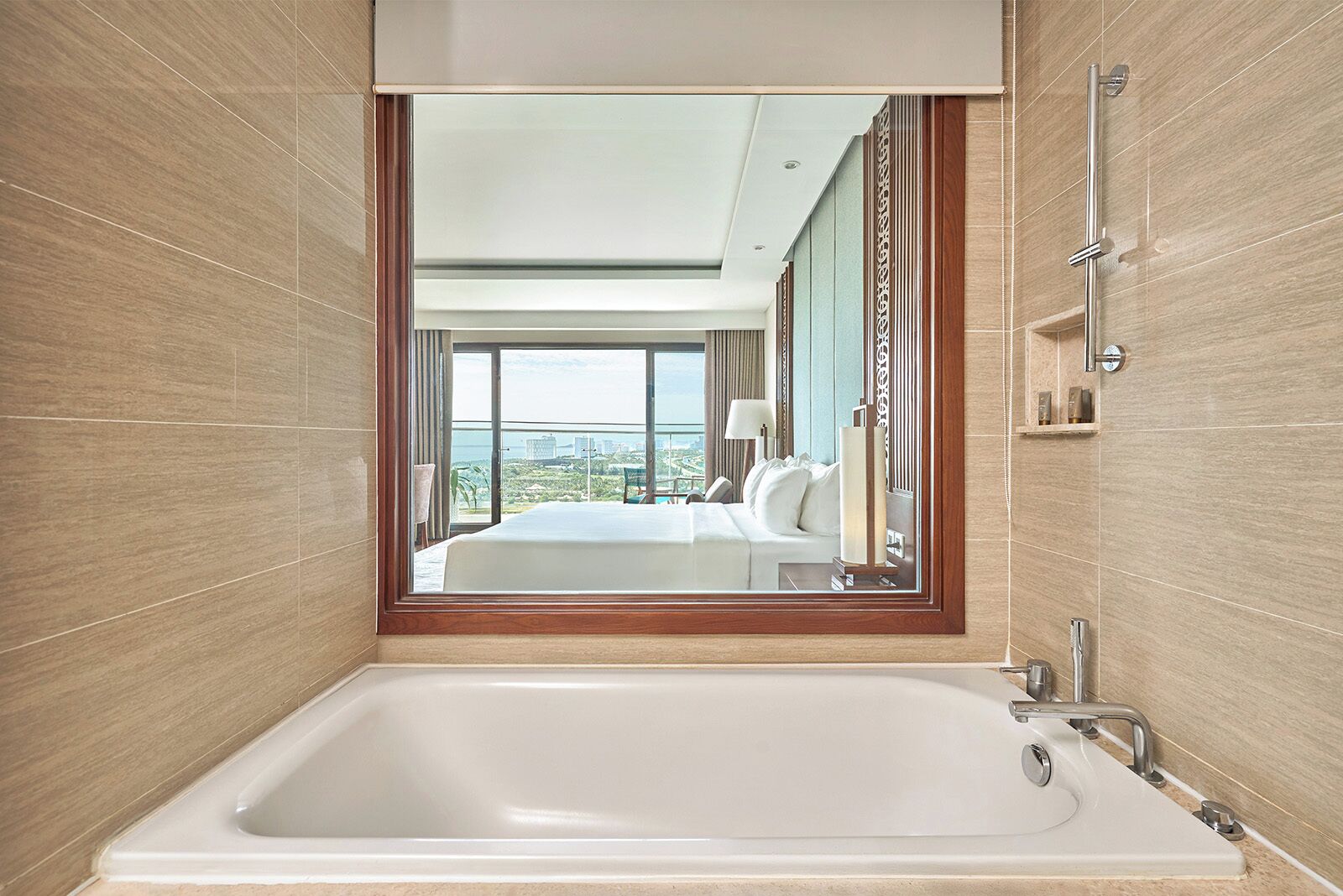 Un bagno moderno con una vasca da bagno ampia, uno specchio che riflette una camera da letto e vista sulla città.