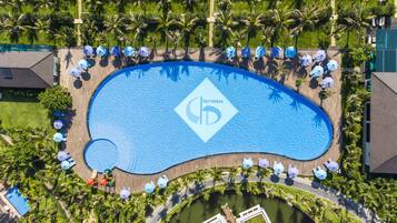 Vista aérea de un resort con una gran piscina, palmeras y una terraza de madera con sombrillas.