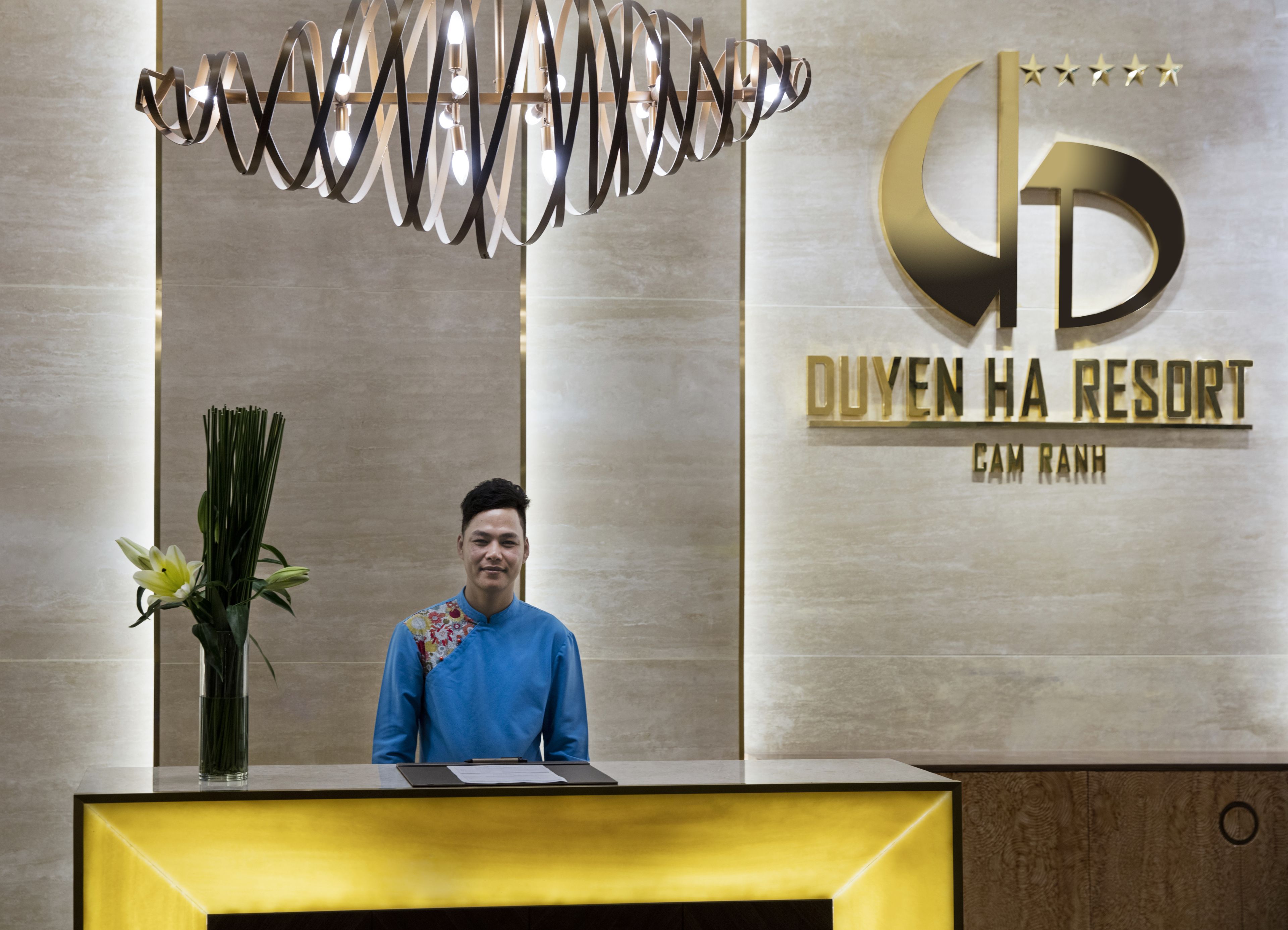 A reception desk with a modern chandelier, a sign for Duven Ha Resort, and a floral arrangement.