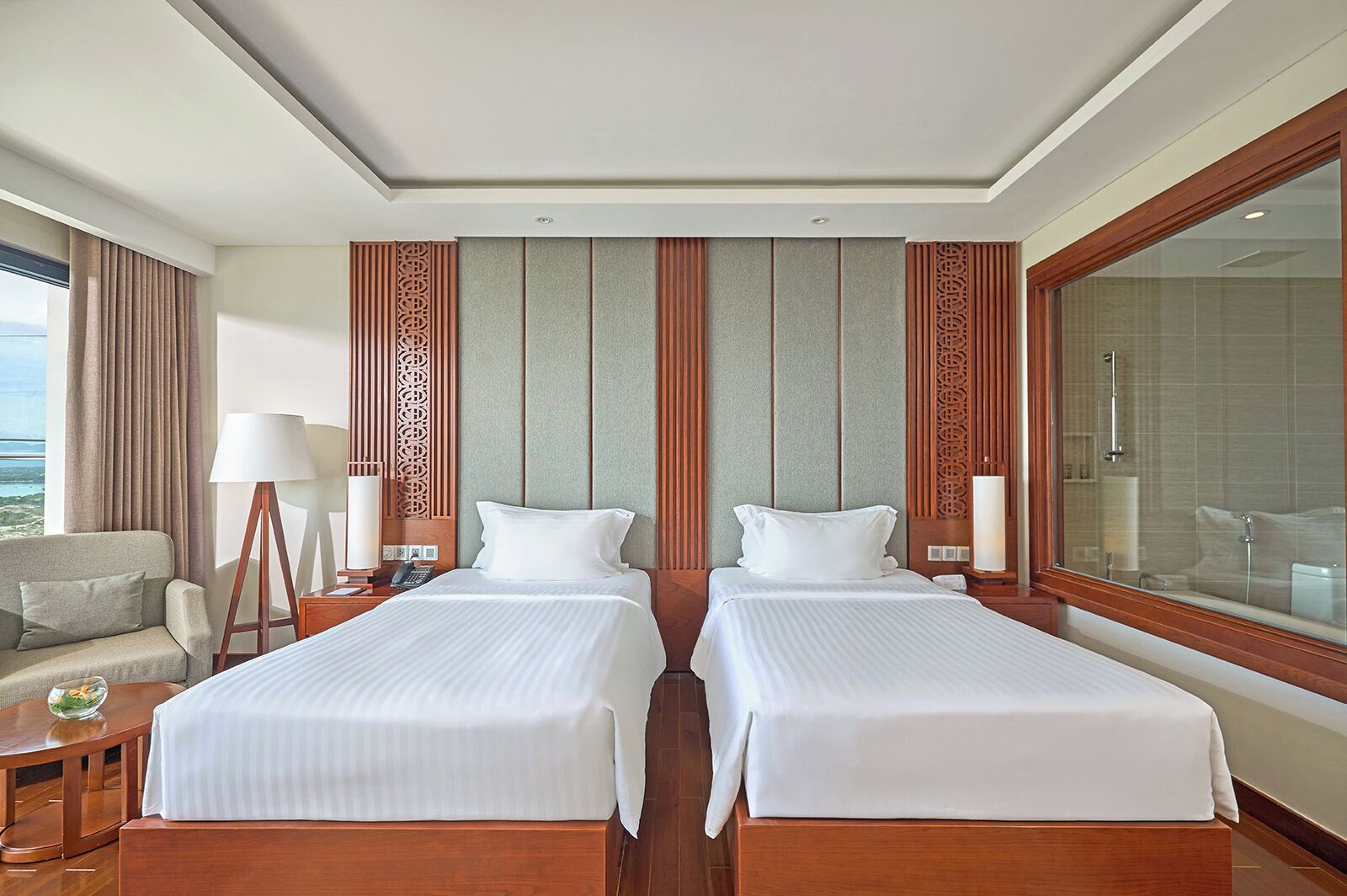 A hotel room with two beds, a sofa, a lamp, a nightstand, and a large window with a view.