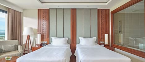 A hotel room with two beds, a sofa, a lamp, a nightstand, and a large window with a view.