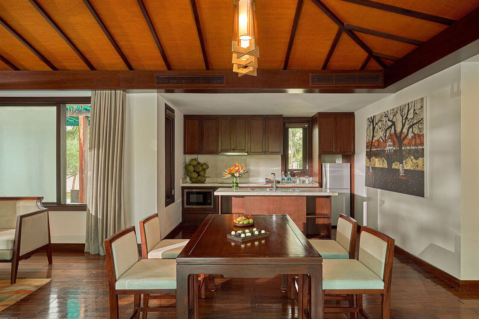 A dining area with a wooden table and chairs, a kitchen with wooden cabinets, and a painting on the wall.