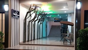 A modern hotel entrance with a staircase, a signboard, and a seating area with a table and chairs. - Smile Resort Thungsong (Thung Song)