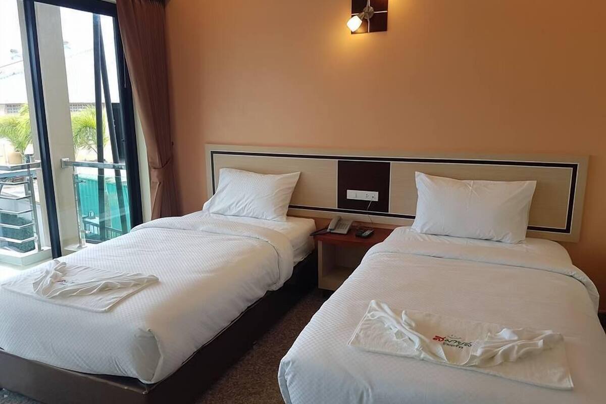 Ein Hotelzimmer mit zwei Betten, einem kleinen Tisch mit Telefon und einer wandmontierten Lampe.