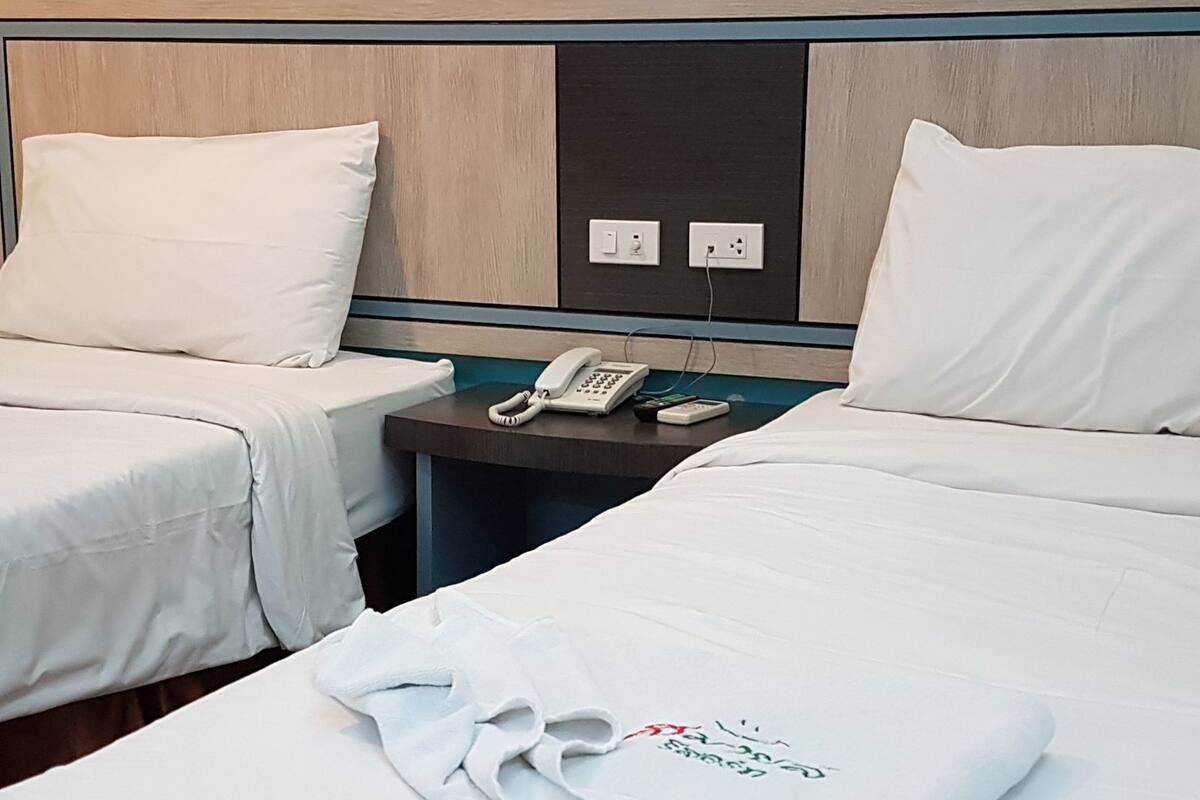 Une chambre d’hôtel avec deux lits, une table de chevet avec un téléphone et une serviette ornée d’un logo.