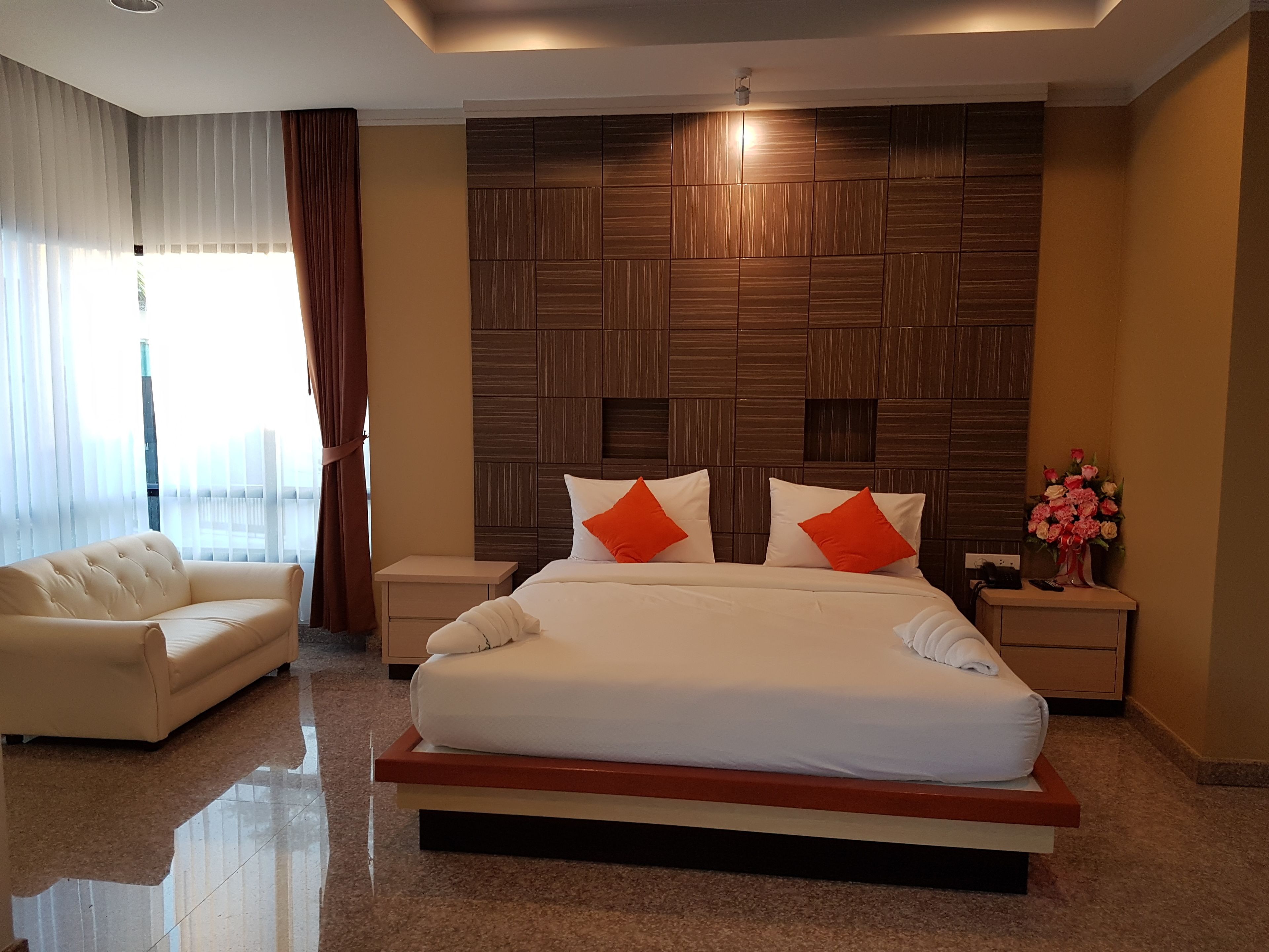 Ein modernes Hotelzimmer mit einem großen Bett, einem Nachttisch, einer Sitzecke und einer dekorativen Vase mit Blumen.