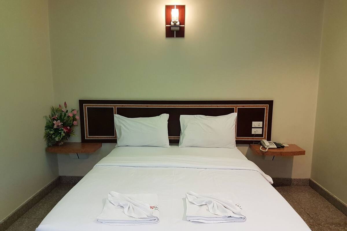 Une chambre d’hôtel avec un lit bien fait, une table de chevet avec une lampe et un luminaire fixé au mur.