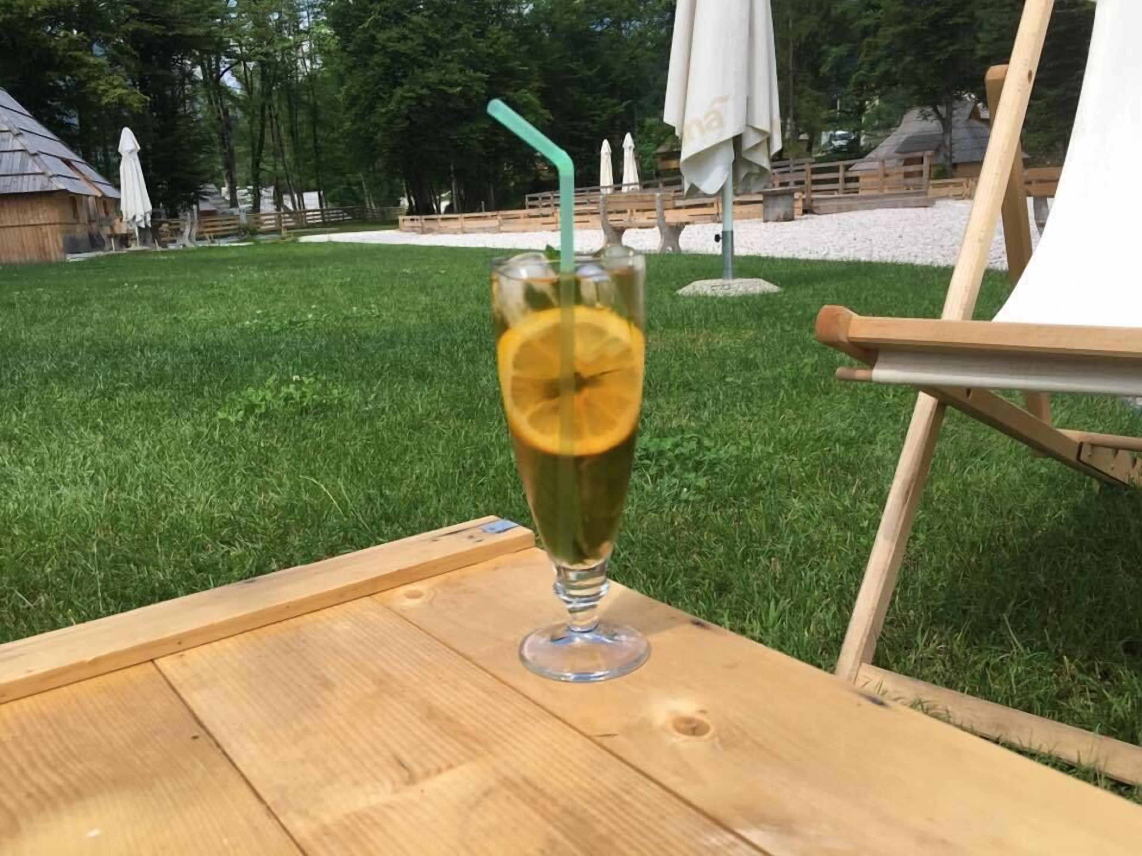 A clear glass with a lemon slice and a straw on a wooden table outdoors.