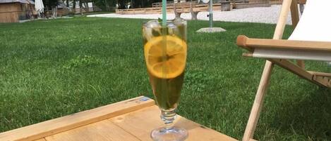 A clear glass with a lemon slice and a straw on a wooden table outdoors.