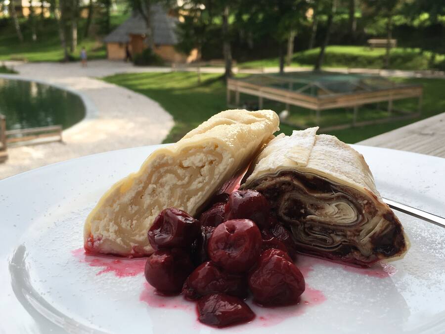 Eine Dessertplatte mit einem Blätterteigröllchen und Kirschen auf einem weißen Teller.