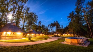 A row of thatched-roof cottages with a hot tub in the foreground. - Slovenia Eco Resort (Kamnik)