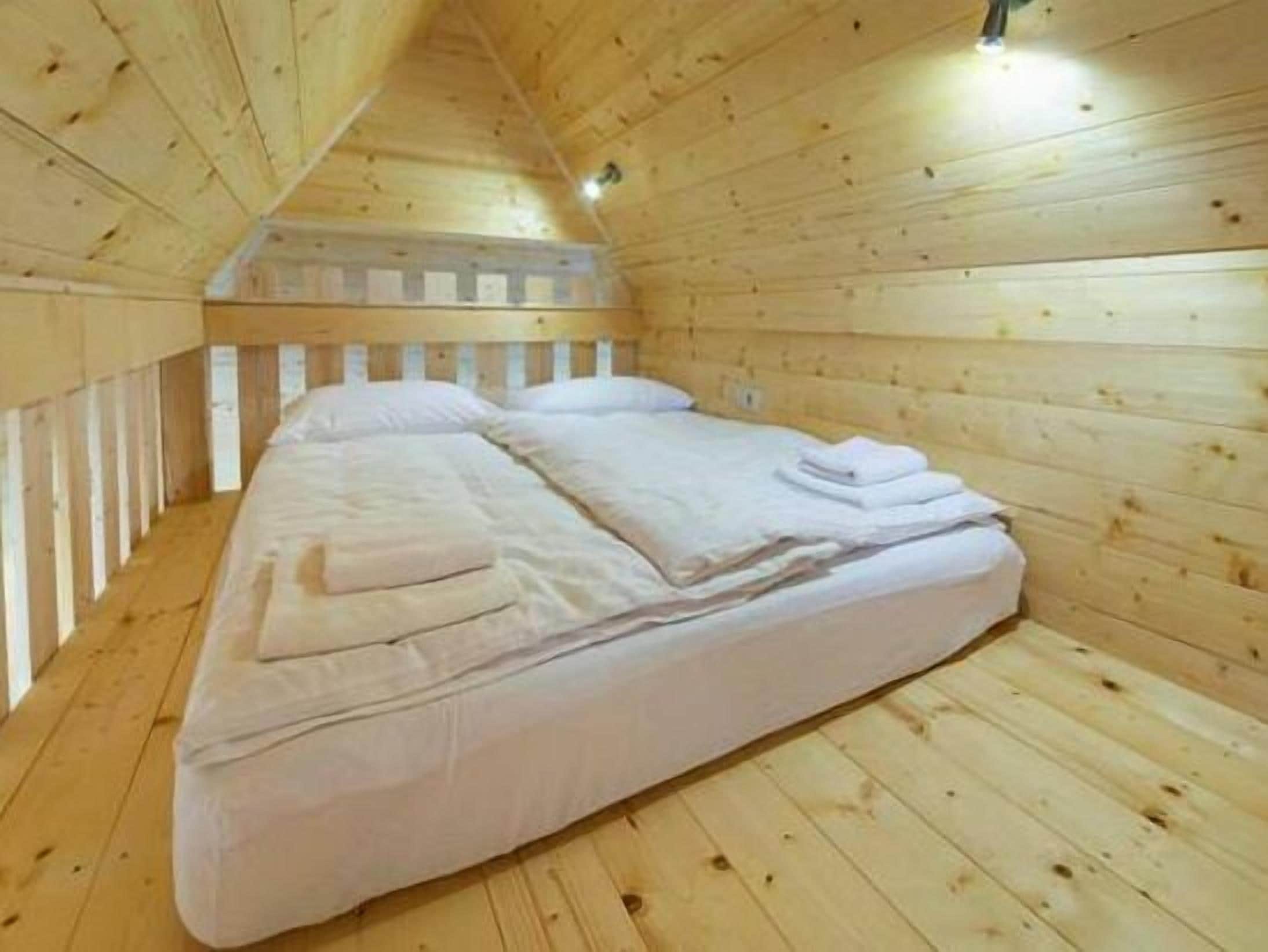 Une pièce de cabane en bois avec un lit simple, des murs en bois et un plafond en pente.