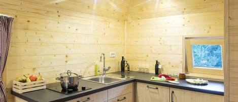 Cocina de una cabaña de madera con encimera negra, armarios de madera, un fregadero y una ventana con vistas a árboles.