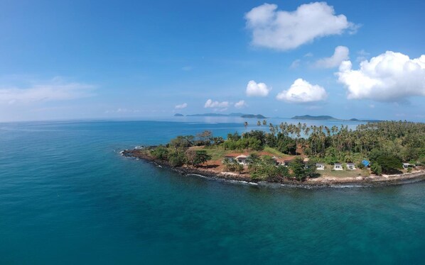 An aerial view of a tropical island with clear blue waters, a small settlement with houses, and palm trees. - Ta-Lay Time KohMak (Ko Mak)