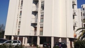 A multi-story building with a central core, balconies on each floor, and a parking area in front. - Residenza Cisanello (Pisa)