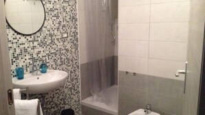 A bathroom with a mosaic tile wall, a round mirror, a sink with two blue soap dispensers, a white towel, a bidet, and a shower enclosure. - Residenza Cisanello (Pisa)