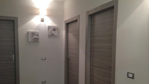 A hallway with two wooden doors, a wall-mounted light fixture, and two wall-mounted light switches. - Residenza Cisanello (Pisa)