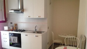 A compact kitchen with a stove, sink, and oven, adjacent to a dining area with a small table and chairs. - Residenza Cisanello (Pisa)