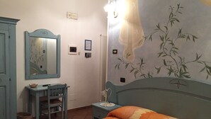 A bedroom with a bed, a desk, a chair, a wardrobe, and a wall with a floral mural. - La Locanda di Giorgia (Pisa)