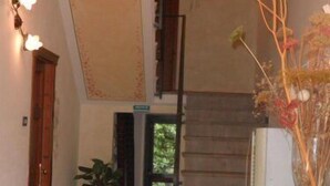 A hallway with a staircase, a wooden door, a potted plant, and a vase with branches. - La Locanda di Giorgia (Pisa)