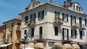Um edifício de vários andares com varandas decoradas com flores, entrada voltada para a rua e toldos sobre as janelas.