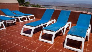 A rooftop terrace with blue lounge chairs and a red-tiled floor.