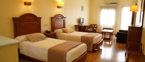 A hotel room with two beds, a desk, a chair, and a TV.