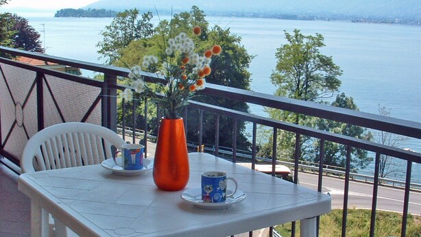 A balcony with a table set for two, a vase with flowers, and a scenic view of a lake and mountains. - Residence Tre Ponti (Verbania)