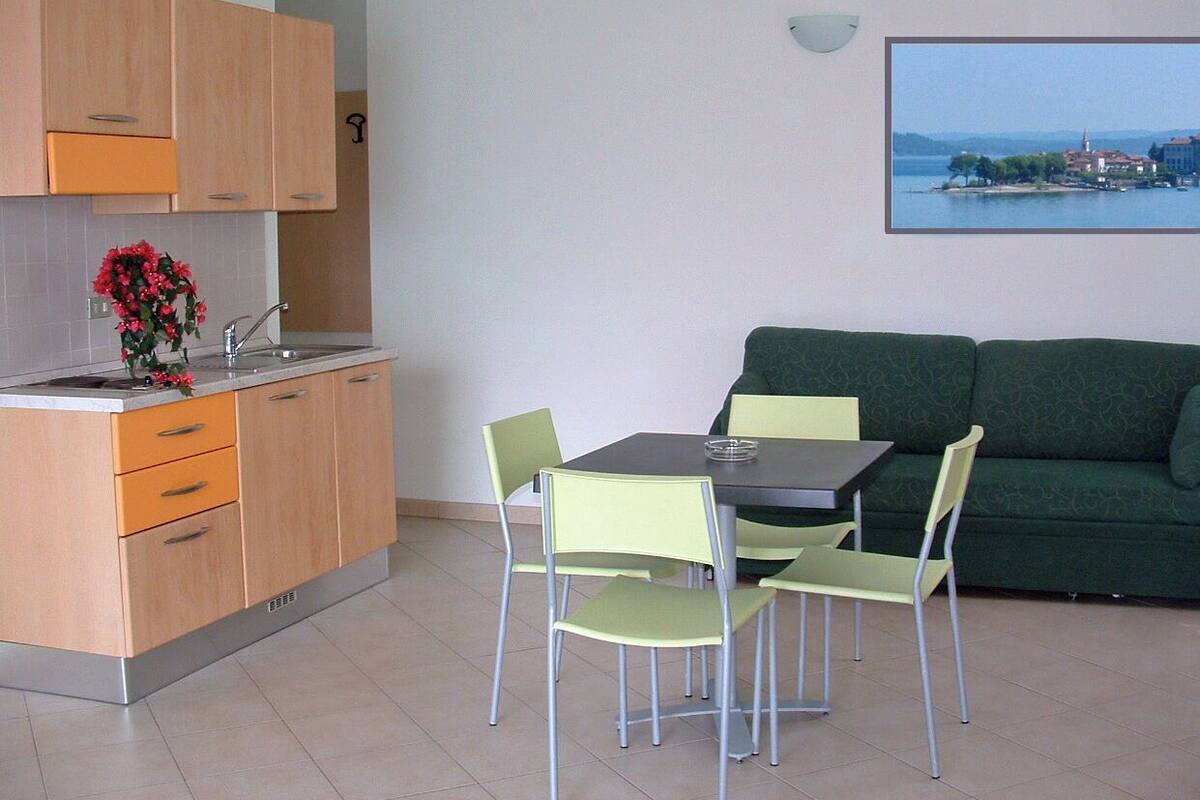 A compact living space with a kitchenette, a dining area with a table and chairs, and a green sofa.