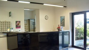 A reception desk with a black counter, a clock on the wall, and a window with a view of greenery outside. - Residence Tre Ponti (Verbania)