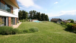 Una casa moderna de dos pisos con piscina, rodeada de césped cuidado y árboles.