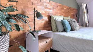 Un dormitorio con cabecera de madera, una mesita de noche con lámpara, una cama con almohadas y una planta en maceta.