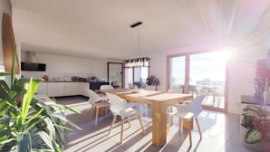 Una cocina moderna con armarios blancos, una mesa de comedor de madera y sillas blancas. Hay un ventanal que ofrece vistas al exterior.