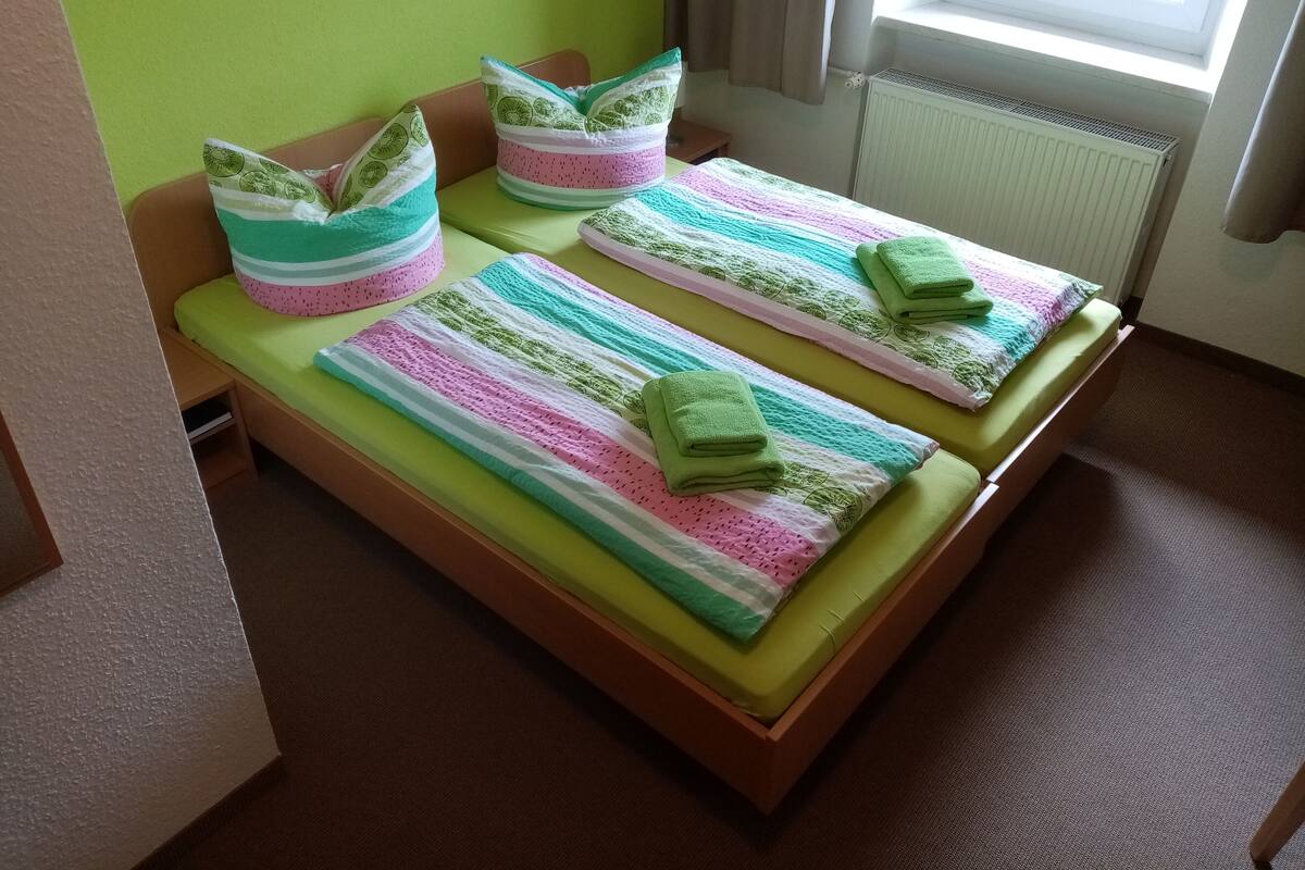 A single bed with a green mattress, striped bedding, and pillows with a leaf pattern.