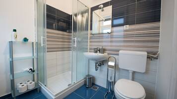 Een moderne badkamer met een douchecabine van glas, een wit wastafelmeubel en een toilet.