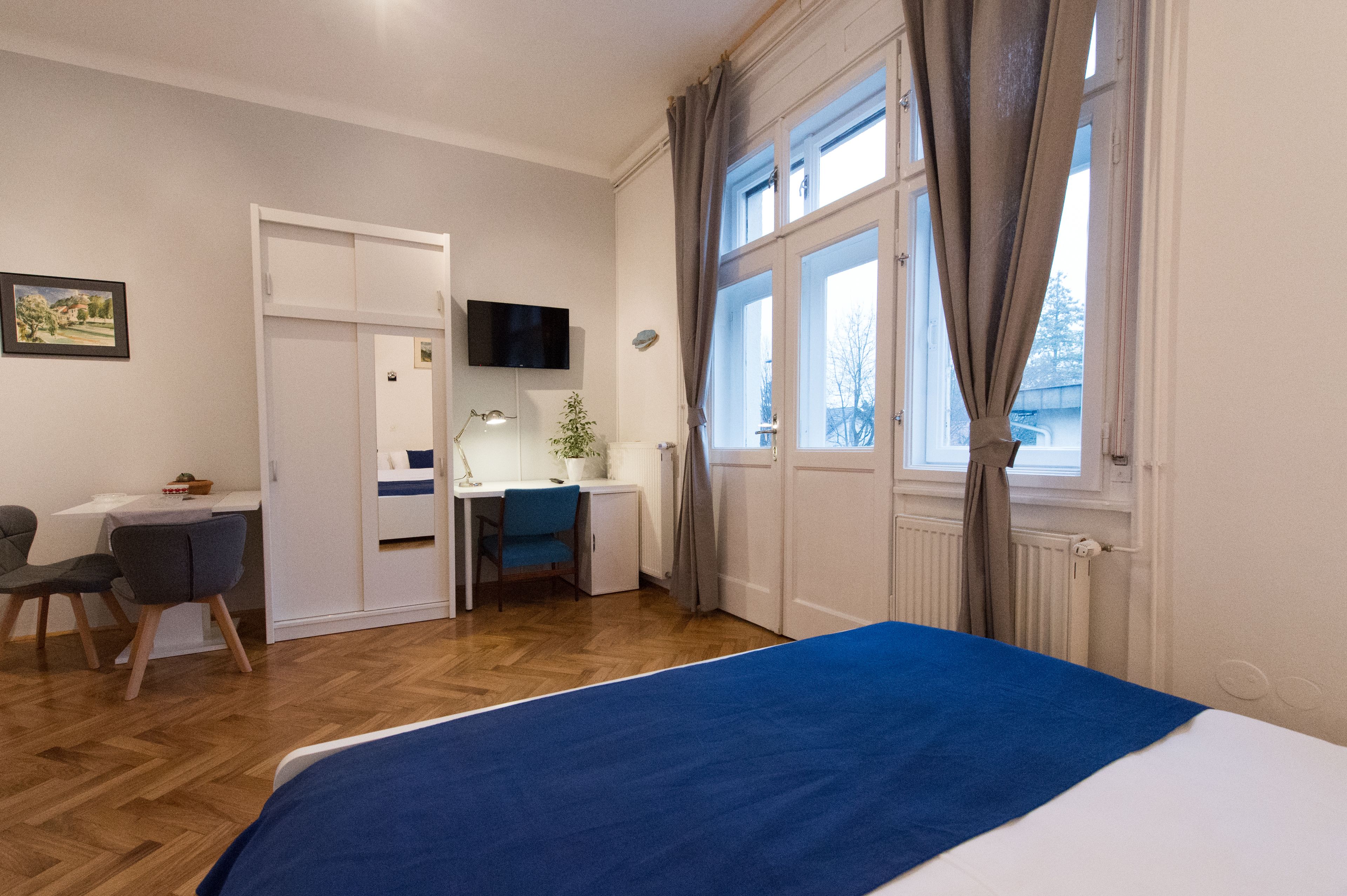 A hotel room with a bed, a desk, a chair, a television, and a window with curtains.
