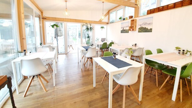 Un amplio comedor con vigas de madera, mesas y sillas blancas.