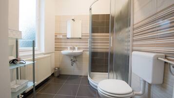 Ein modernes Badezimmer mit einer Glaskabine zur Dusche, einer weißen Toilette, einem Waschbecken und einem Fenster, das natürliches Licht hereinlässt.